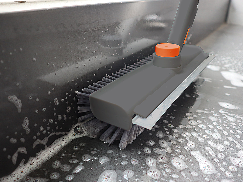 Cleaning brush with an orange handle scrubbing a car's black surface.